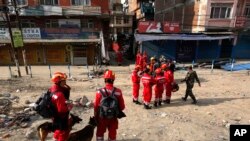 Satu tim SAR dari China bersama anjing pelacak berdiri di dekat sebuah gedung yang rusak akibat gempa di Kathmandu, Nepal, 26 April 2015 (AP Photo / Manish Swarup).