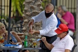 A food server wearing a protective face mask waits on customers at the Parkshore Grill restaurant in St. Petersburg, Fla., May 4, 2020.