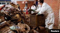 A woman piles up damaged toys outside a toy shop affected by heavy rains at a shopping centre, in Sedavi, Valencia, Spain.