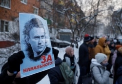 A man holds a placard reading "For Navalny!" as people, including supporters of Alexei Navalny, gather outside a police station where the Russian opposition leader is being held following his detention, in Khimki, Russia, January 18, 2021.