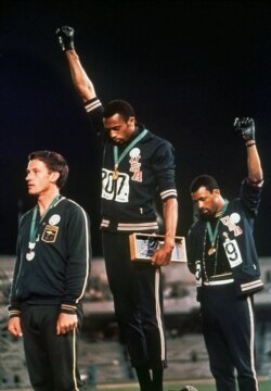 FILE - Extending gloved hands skyward in racial protest, U.S. athletes Tommie Smith, center, and John Carlos stare downward during the playing of "The Star-Spangled Banner" in the 1968 Mexico City Games.