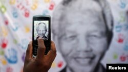 A well-wisher takes a picture of a banner with the image of former South African President Nelson Mandela, outside the hospital where he is being treated, in Pretoria, July 18, 2013.