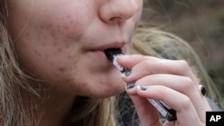 FILE - A high school student uses a vaping device near a school campus in Cambridge, Mass.