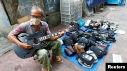 Seorang penjaja dagangan bermain gitar sambil menunggu pembeli di pinggir jalan di tengah pandemi Covid-19 di Jakarta, 21 April 2020. 