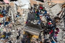 People look for goods while an excavator removes rubble from a destroyed building after Saturday's 7.2 magnitude quake, in Les Cayes, Haiti, August 18, 2021.