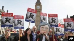 Demonstrators, one dressed in a Theresa May puppet head pose near parliament in London, March 13, 2017.