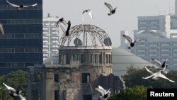 Burung merpati beterbangan di atas Taman Memorial Perdamaian di Hiroshima dengan Kubah Bom Atom pada latar belakang.