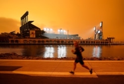 FILE - Under darkened skies from wildfire smoke, a jogger makes his way along McCovey Cove outside Oracle Park, Sept. 9, 2020, in San Francisco.