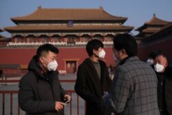 People wearing protective masks stand outside the entrance of the Forbidden City where a notice says the place is closed to visitors following the outbreak of a new coronavirus, in Beijing, China, Jan. 25, 2020.