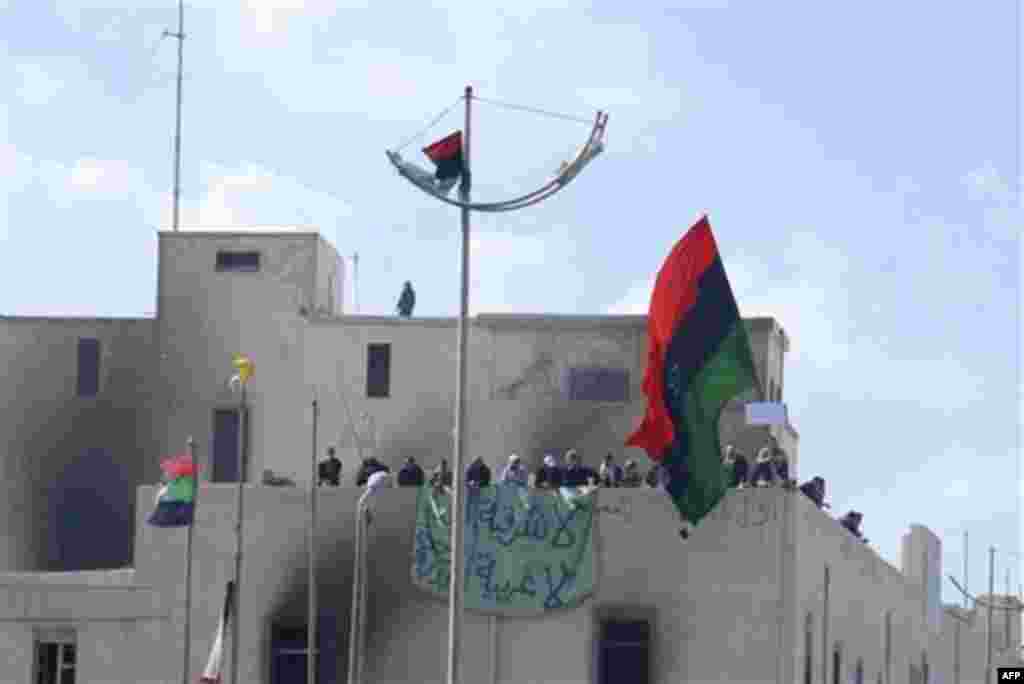 This photograph, obtained by The Associated Press outside Libya and taken by an individual not employed by AP, shows people atop a building holding a banner and a flag during recent days' unrest in Benghazi, Libya. The graffiti in Arabic reads "No to the 