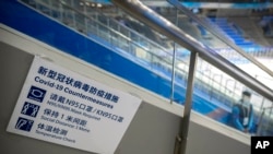 FILE - A staff member stands near a sign outlining COVID-19 protection measures during the Experience Beijing Ice Hockey Domestic Test Activity, a test event for the 2022 Beijing Winter Olympics, at the National Indoor Stadium in Beijing, on Nov. 10, 2021