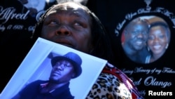 FILE - A woman holds a picture of Alfred Olango as she listens to speeches during an Oct. 1, 2016, rally and march to protest the fatal police shooting of the Ugandan immigrant in El Cajon, California, four days earlier.