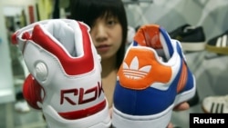 A saleswoman holds up athletic shoes by Reebok and Adidas in Taipei August 4, 2005.