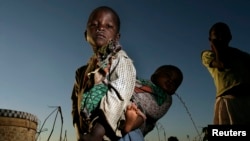 FILE - A young girl carries her sister through a cornfield in Masongo village outside Lilongwe, Malawi, May 13, 2008. 