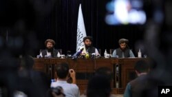 FILE - In front of a Taliban flag, Taliban spokesman and now the group's deputy culture and information Minister Zabihullah Mujahid, center, speaks at a news conference, in Kabul, Afghanistan, Aug. 17, 2021. 