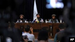 In front of a Taliban flag, Taliban spokesman Zabihullah Mujahid, center, speaks at his first news conference, in Kabul, Afghanistan, Aug. 17, 2021. 