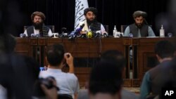 In front of a Taliban flag, Taliban spokesman Zabihullah Mujahid, center, speaks at his first news conference, in Kabul, Afghanistan, Aug. 17, 2021. 