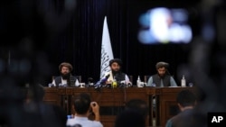 Frente a una bandera talibán, el portavoz talibán Zabihullah Mujahid, centro, habla en su primera conferencia de prensa, en Kabul, Afganistán, el 17 de agosto de 2021.