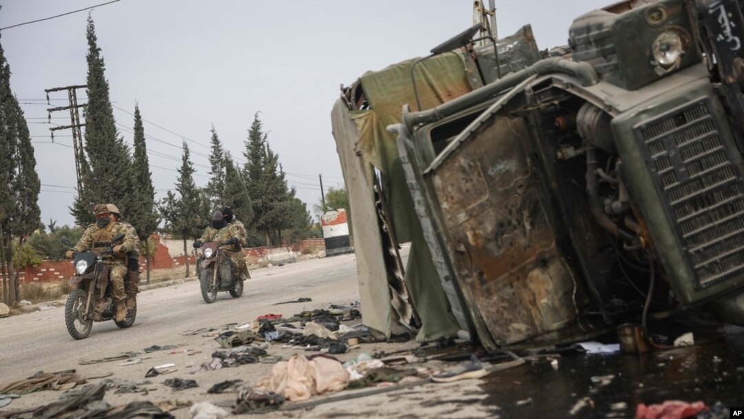 Syrian opposition fighters drive past a damaged government vehicle south of Hama, Syria, Dec. 7, 2024.