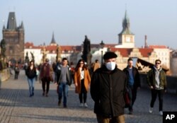 FILE - A man wearing a face mask to guard against coronavirus transmission walks across the medieval Charles Bridge in Prague, Czech Republic, Feb. 25, 2021.