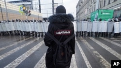 FILE - A man with a sign "Navalny" on his back stands in front of riot policemen blocking the way during a protest against the jailing of opposition leader Alexey Navalny in St. Petersburg, Russia, Jan. 31, 2021. 