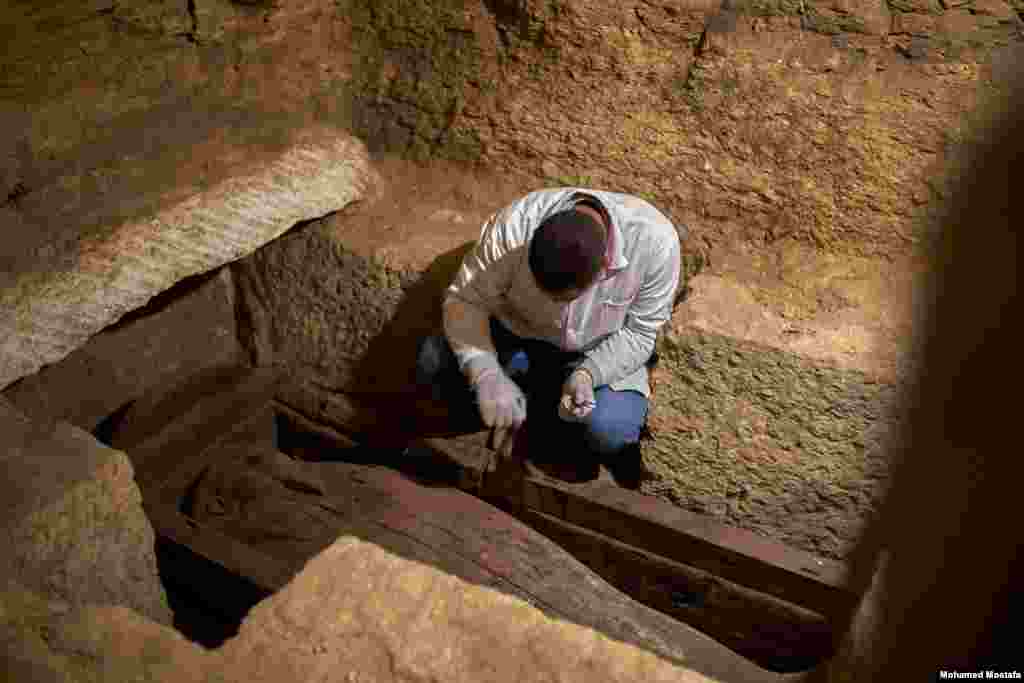 Egyptian archaeologist Ashraf Saad provides first aid to one of 5 wooden coffins found at the Al-Ghoreifa area of the Tuna El-Gabal archaeological site in Minya, Egypt. (Hamada Elrasam/VOA)