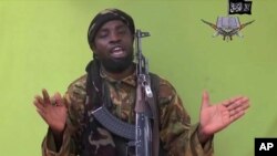 រូបភាព​យក​ចេញ​ពី​វីដេអូ​ក្រុម​ Boko Haram នៅ​នីហ្សេរីយ៉ា​នៅ​ក្នុង​ខែ​ឧសភា​ឆ្នាំ​ ២០១៤​ ដែល​បង្ហាញ​មេដឹកនាំ​ Abubakar Shekau​។ ក្រុម​ Boko Haram​ ប្តេជ្ញា​ស្មោះ​ស្ម័គ្រ​នឹង​ក្រុម​រដ្ឋអ៊ីស្លាម​​។