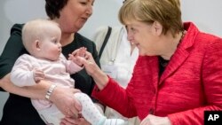 FILE - German chancellor Angela Merkel sshares a smile with the ten-month-old baby Romy at an event celebrating the 15th anniversary of the family support organization 'Wellcome ' in Berlin, March 6, 2017. 