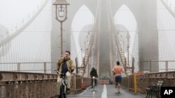 Dua orang pengendara sepeda dan seorang pelari melewati jembatan Brooklyn di New York, dalam cuaca berkabut (23/12). Suhu udara musim dingin di seluruh Amerika menjadi hangat akibat El Nino.