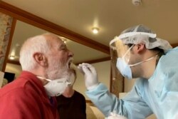 FILE - In this image from a video, Paul Molesky, left, gets a DNA swab test in his cabin room on the Diamond Princess, anchored at a port in Yokohama, near Tokyo, Feb. 13, 2020.