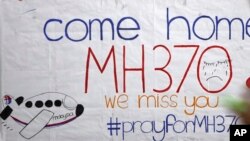 A woman stands in front of a placard featuring messages for passengers aboard a missing Malaysia Airlines plane at Kuala Lumpur International Airport in Sepang, Malaysia, March 12, 2014. 