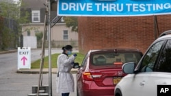 FILE - Medical personnel prepare to administer a COVID-19 swab at a drive-through testing site in Lawrence, New York, Oct. 21, 2020.