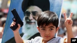 FILE - An Iraqi boy living in Iran holds a toy gun and flashes a victory sign in front of a poster of Iranian supreme leader Ayatollah Ali Khamenei in demonstration against Sunni militants of the Islamic State group in Tehran, June 20, 2014.