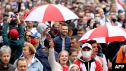 Opposition supporters carrying umbrellas in the colors of a former white-red-white fag of Belarus parade through the streets during a rally to protest against the presidential inauguration in Minsk, Sept. 27, 2020. 