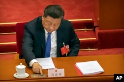 FILE - Chinese President Xi Jinping reaches to vote on a piece of national security legislation concerning Hong Kong during the closing session of China's National People's Congress in Beijing, May 28, 2020.