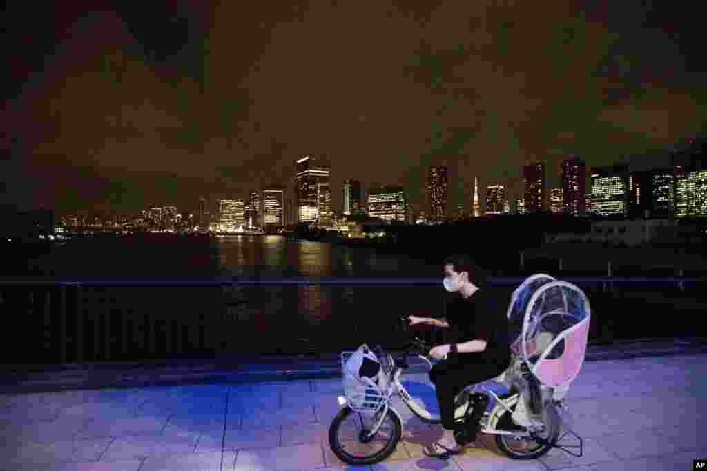 일본 도쿄의 야경을 뒤로 한 여성이 신종 코로나바이러스 감염 예방을 위한 마스크를 쓴 채 자전거를 타고 있다. 