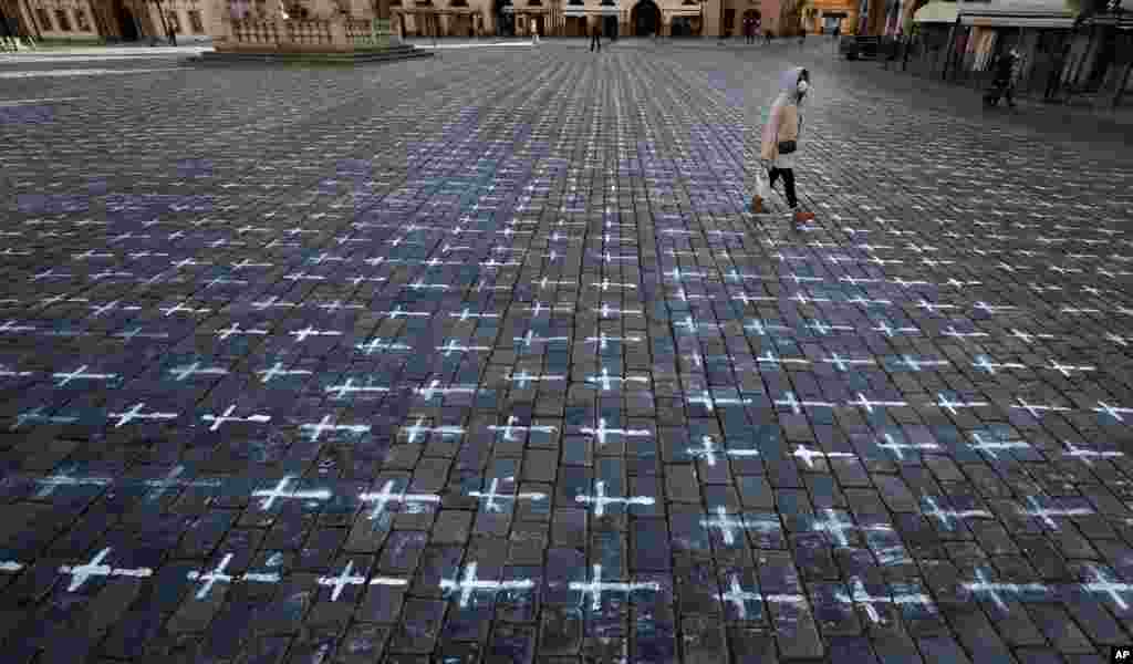 A woman walks at the Old Town Square in Prague, Czech Republic. Thousands of crosses have been painted on a pavement to commemorate the first anniversary since the death of the first COVID-19 patient.