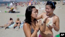 FILE - Kristi Moy, right, helps Kinari Sakamoto apply sunscreen June 21, 2012. The U.S. Food and Drug Administration, or FDA, reported recently that the chemicals are present at much higher levels than current government health rules permit. (AP Photo/Seth Wenig)