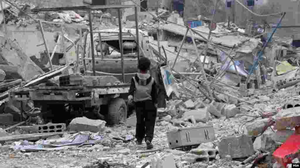 Yaro dan Syria yana tafiya a gefen burbushi da wata lalataciyyar mota a kauyen Hazzeh dake gabashin Ghouta a wajen garin Damascuss. 