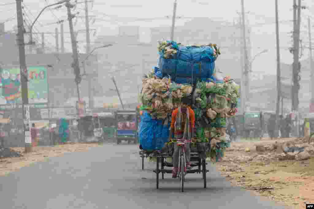 A Bangladeshi man cycles his loaded-up rickshaw next to the Buriganga River in Dhaka.