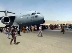 Hundreds of people run alongside a U.S. Air Force C-17 transport plane as it moves down a runway of the international airport, in Kabul, Afghanistan, Aug.16. 2021.