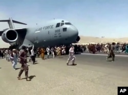 FILE - Hundreds of people run alongside a U.S. Air Force C-17 transport plane as it moves down a runway of the international airport, in Kabul, Afghanistan, Aug.16. 2021.