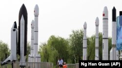 FILE - A woman walks with a child as they visit a park displaying replicas of foreign and domestic space vehicles in Beijing, China, June 26, 2016. 