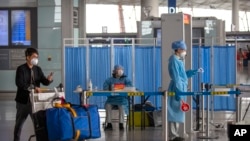 A man pushes his luggage past workers in protective suits as they wait to take the temperature of travelers at Beijing Capital International Airport in Beijing, March 6, 2020.