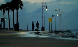 A couple walks along the shore of Lake Pontchartrain at dusk, Aug. 28, 2021, in New Orleans. Hurricane Ida is set to hit the area Sunday as a Category 4 storm.
