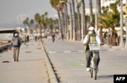 A person wears a mask because of hazardous air quality due to wildfires as she rides her bike by the beach in Santa Monica, California, on Jan. 8, 2025.