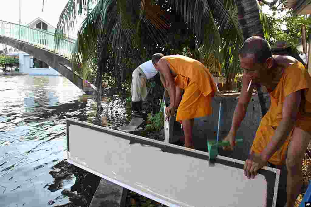 Monks moving sandbags and plywood to shore up river defenses, October 27, 2011. (VOA - D. Schearf)
