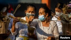 Pemuka agama Hindu menyiram air suci dalam ritual Ngeplugin pada upacara persemayaman Ngaben Ngerit di mana 36 jasad yang meninggal akibat COVID-19 dikremasi dalam upacara yang dilaksanakan di Pura Prajapati di Palu, pada 7 Oktober 2021. (Foto: Antara via Reuters/Basri Marzuki)