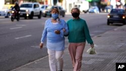 Dos mujeres usando mascarillas para prevenir la diseminación del coronavirus caminan del brazo por una calle del centro de Montevideo, Uruguay, el 19 de mayo de 2020.