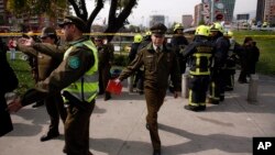 Police officer direct the curious away from a blast site as fire fighters stand by, at a subway station in Santiago, Chile, Sept. 8, 2014.
